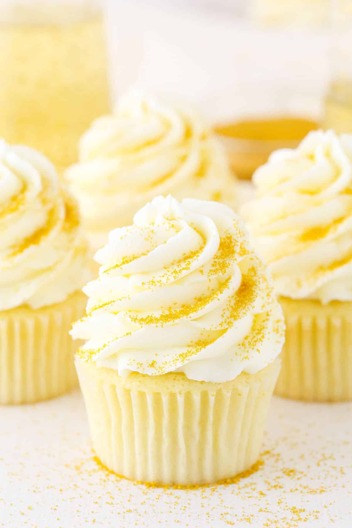 These Champagne Cupcakes are super moist and full of satisfying champagne flavor! They’d be perfect For New Year’s Eve or any other special occasion. Four Champagne Cupcakes decorated with buttercream frosting on a white table top