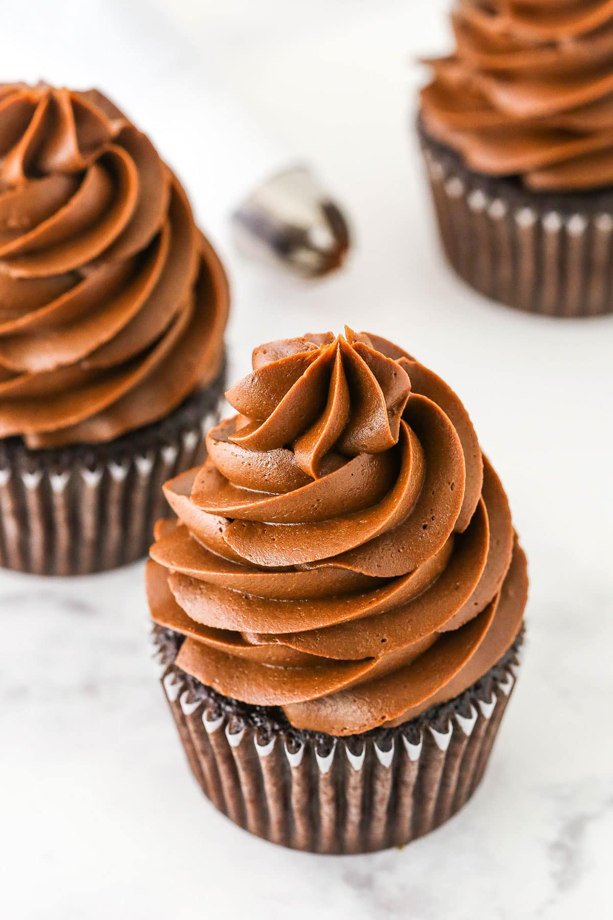 Overhead view of three chocolate cupcakes topped with Chocolate Buttercream Frosting on a white marble table