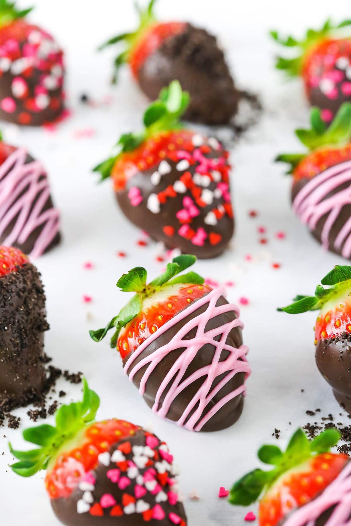 Chocolate Covered Strawberries spread out on a white table top and decorated with pink frosting or red, white and pink sprinkles