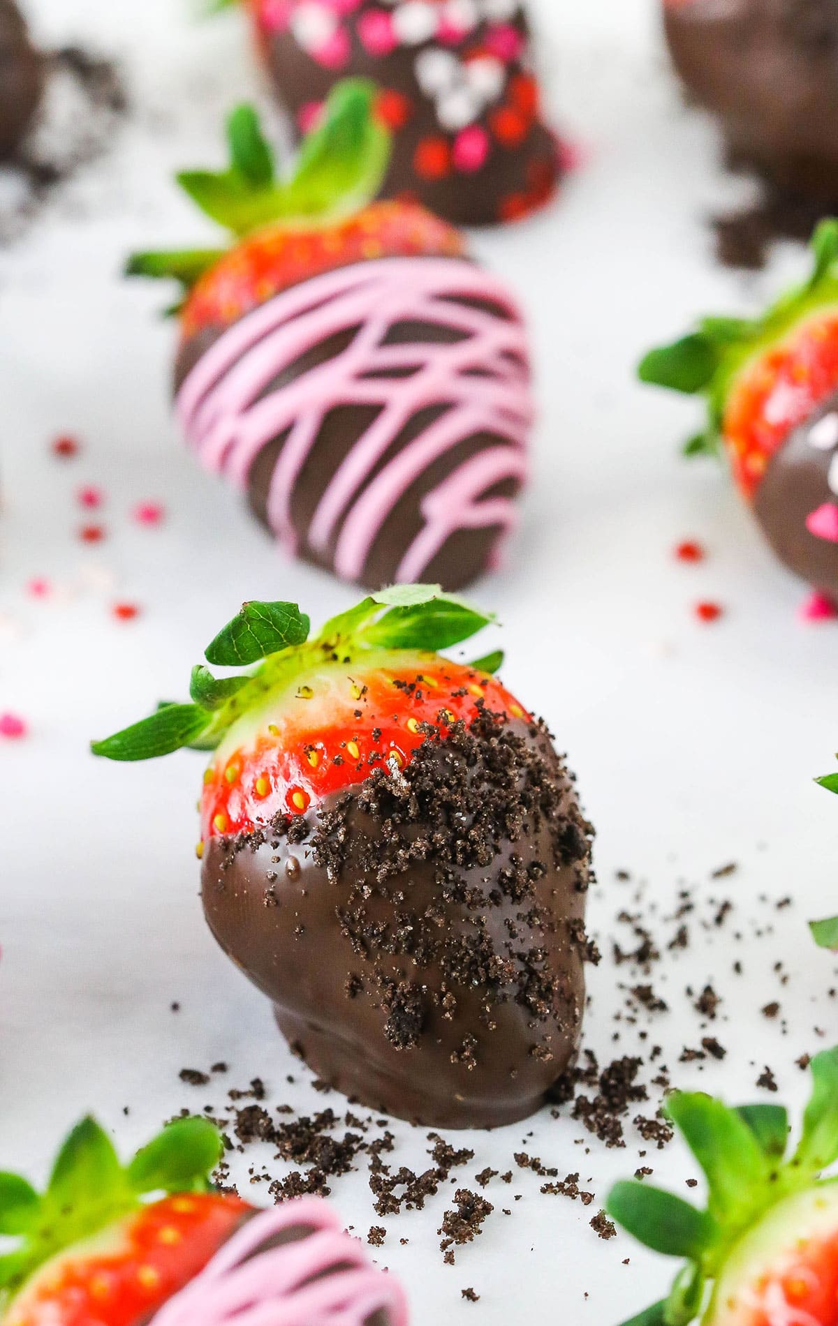 Chocolate Covered Strawberries spread out on a white table top and decorated with pink frosting or red, white and pink sprinkles