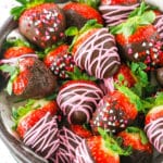 Chocolate Covered Strawberries decorated with pink frosting or red, white and pink sprinkles stacked in a glass bowl on a white table top
