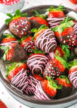 Chocolate Covered Strawberries decorated with pink frosting or red, white and pink sprinkles stacked in a glass bowl on a white table top