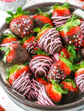 Chocolate Covered Strawberries decorated with pink frosting or red, white and pink sprinkles stacked in a glass bowl on a white table top