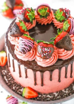 Overhead view of a full Chocolate Covered Strawberry Layer Cake topped with chocolate drip, pink swirls and chocolate covered strawberries on a metal cake stand