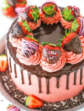 Overhead view of a full Chocolate Covered Strawberry Layer Cake topped with chocolate drip, pink swirls and chocolate covered strawberries on a metal cake stand