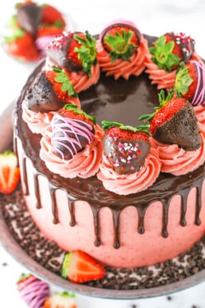 Overhead view of a full Chocolate Covered Strawberry Layer Cake topped with chocolate drip, pink swirls and chocolate covered strawberries on a metal cake stand