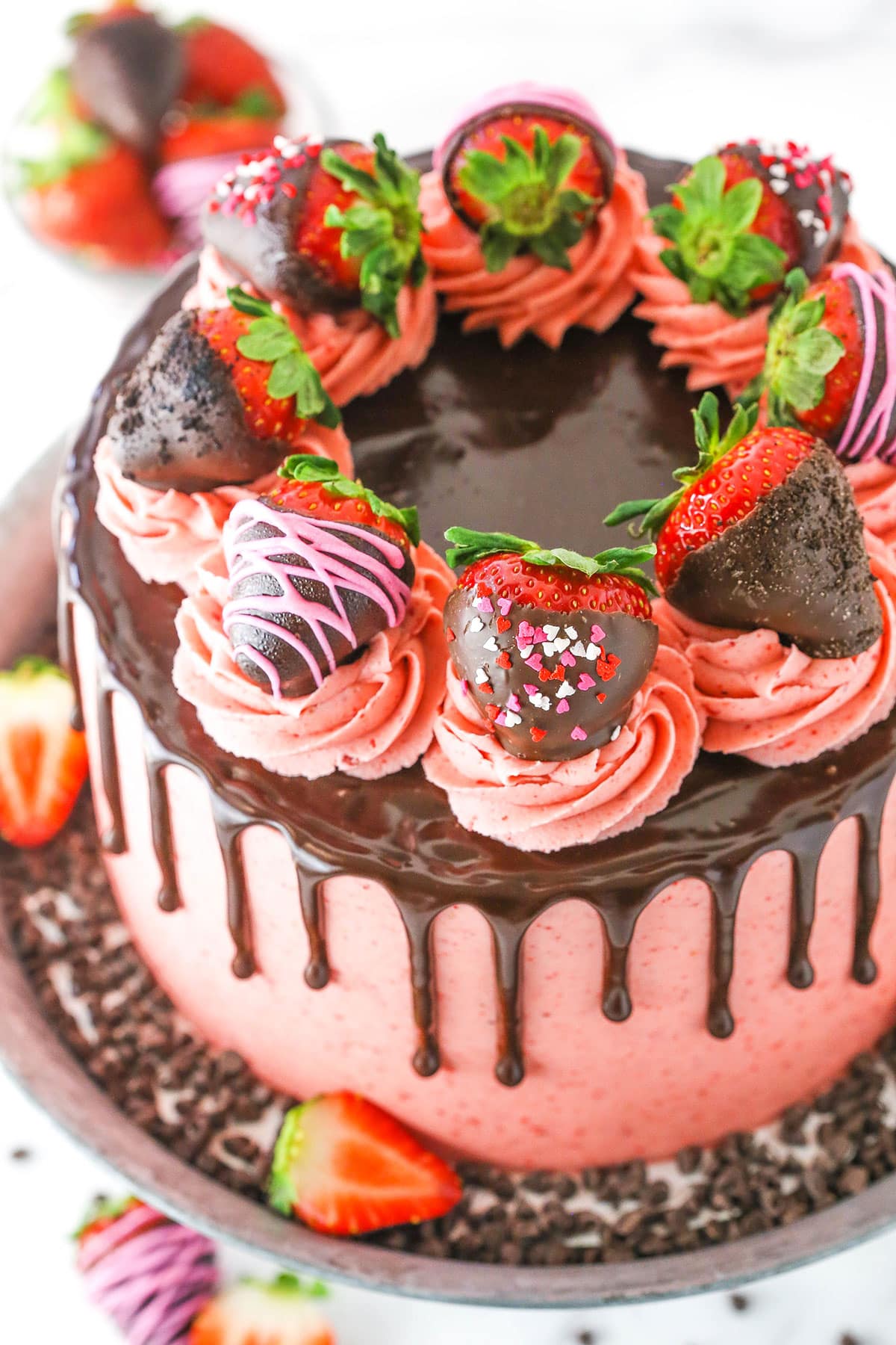 Overhead view of a full Chocolate Covered Strawberry Layer Cake topped with chocolate drip, pink swirls and chocolate covered strawberries on a metal cake stand