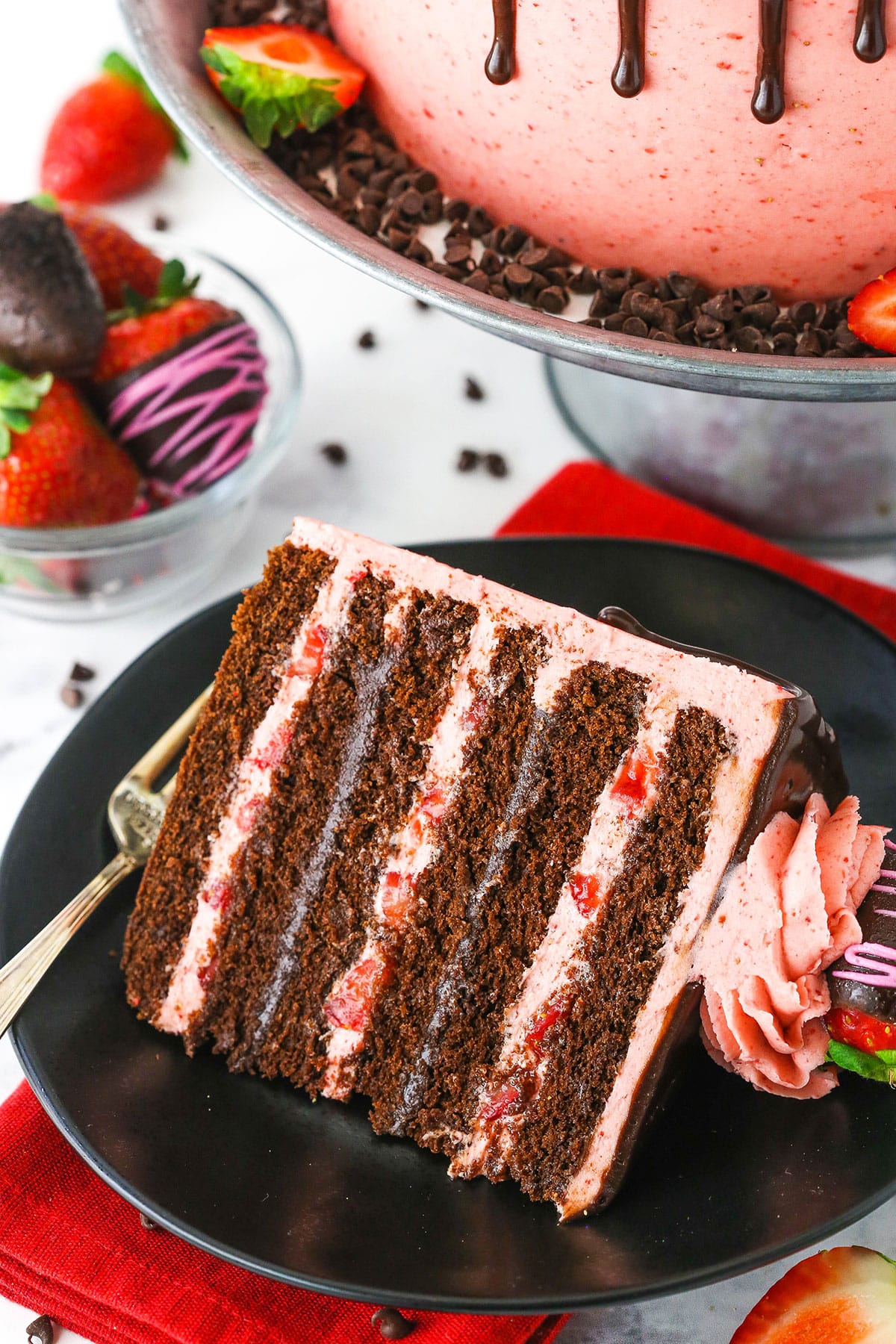 A slice of Chocolate Covered Strawberry Layer Cake on a black plate with a fork