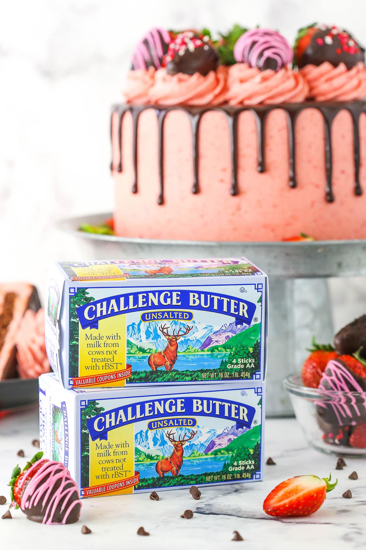 Two boxes of Challenge Butter stacked on a white marble table top with a Chocolate Covered Strawberry Layer Cake on a cake stand in the background