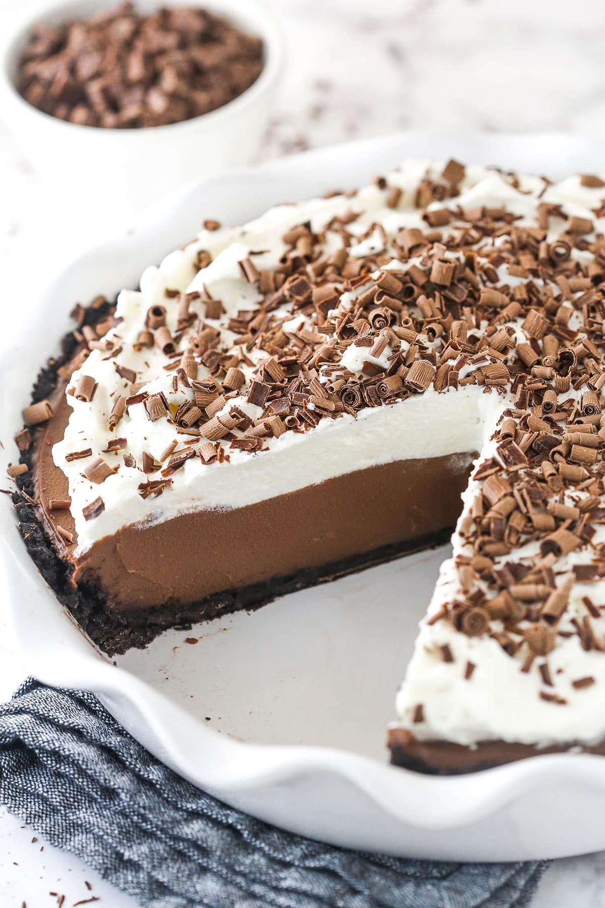 A chocolate cream pie in a serving dish with a slice taken out of it.