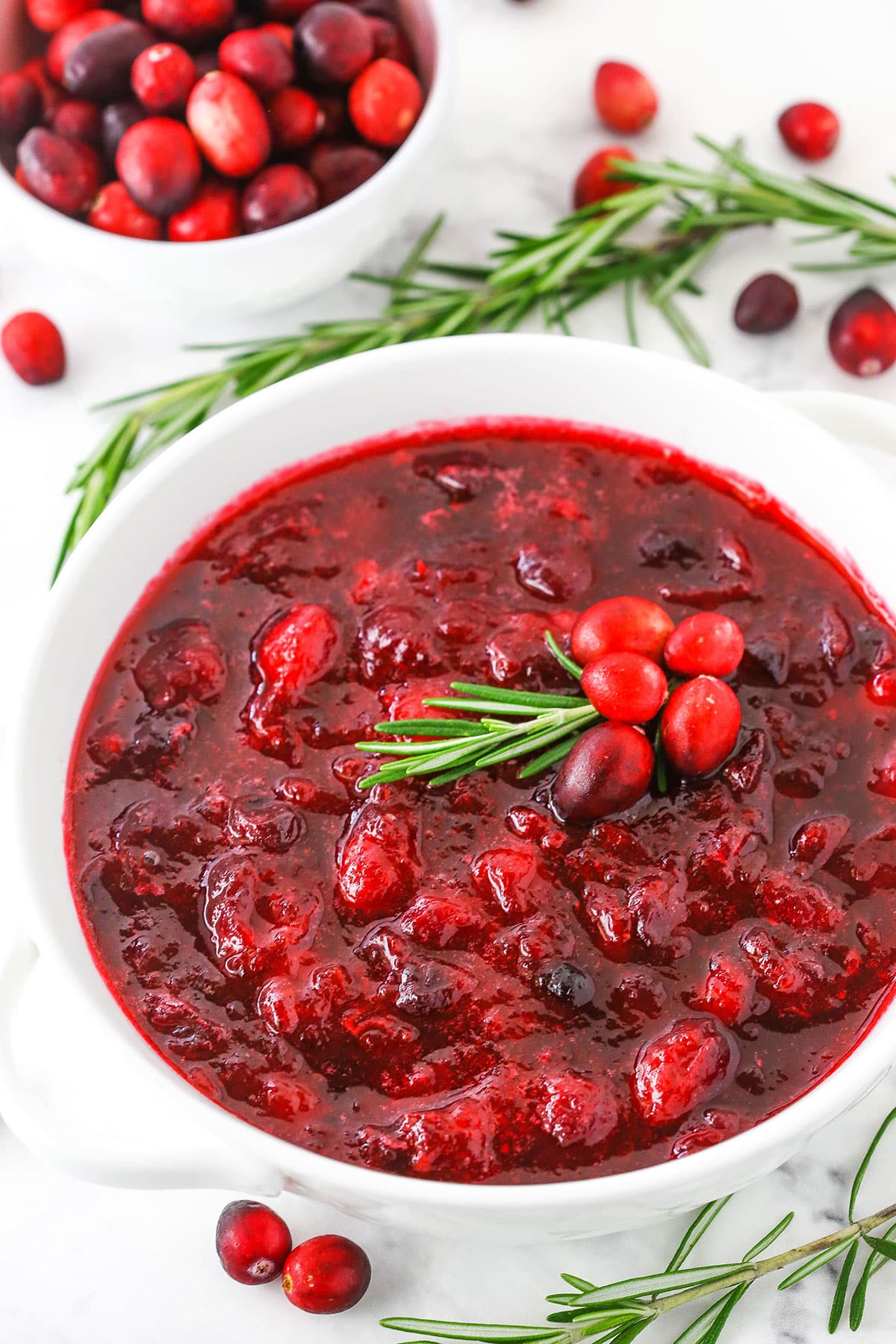 This homemade Cranberry Sauce only has 4 ingredients and is easy to make. It's WAY better than any store-bought version! Plus, it only takes 20 min to make and can be made ahead - perfect for a busy holiday season! Overhead view of easy homemade Cranberry Sauce in a white bowl on a white table