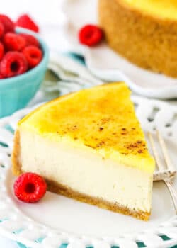 A slice of Creme Brûlée Cheesecake on a white plate with a fork and a raspberry