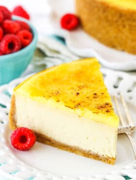 A slice of Creme Brûlée Cheesecake on a white plate with a fork and a raspberry