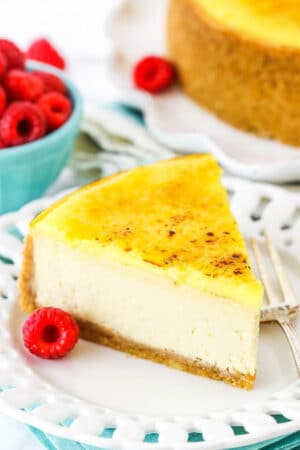 A slice of Creme Brûlée Cheesecake on a white plate with a fork and a raspberry