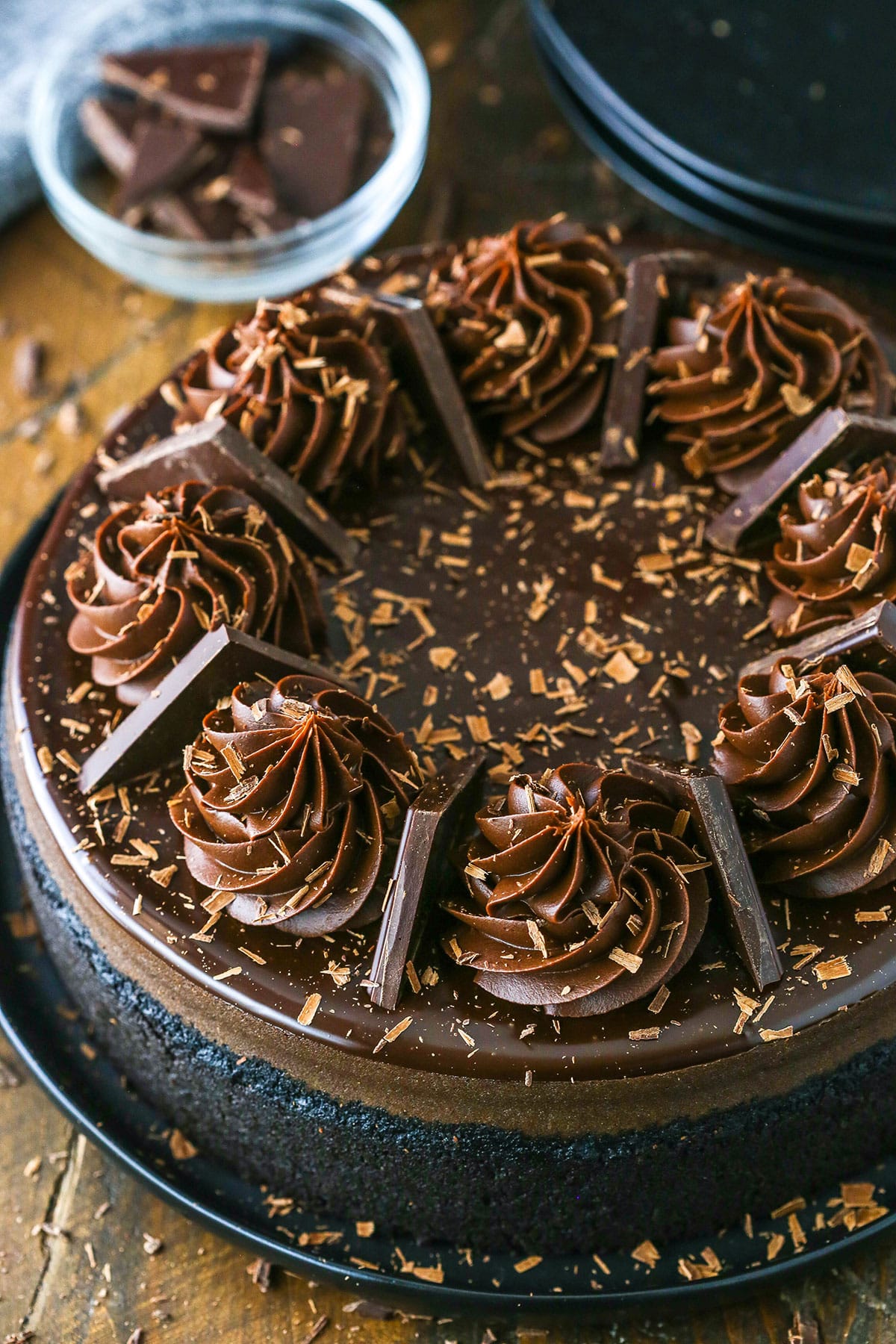 Overhead view of a full Decadent Dark Chocolate Cheesecake topped with dark chocolate ganache swirls and pieces of dark chocolate.