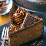 A slice of Decadent Dark Chocolate Cheesecake on a black plate next to a fork