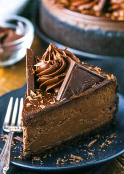 A slice of Decadent Dark Chocolate Cheesecake on a black plate next to a fork