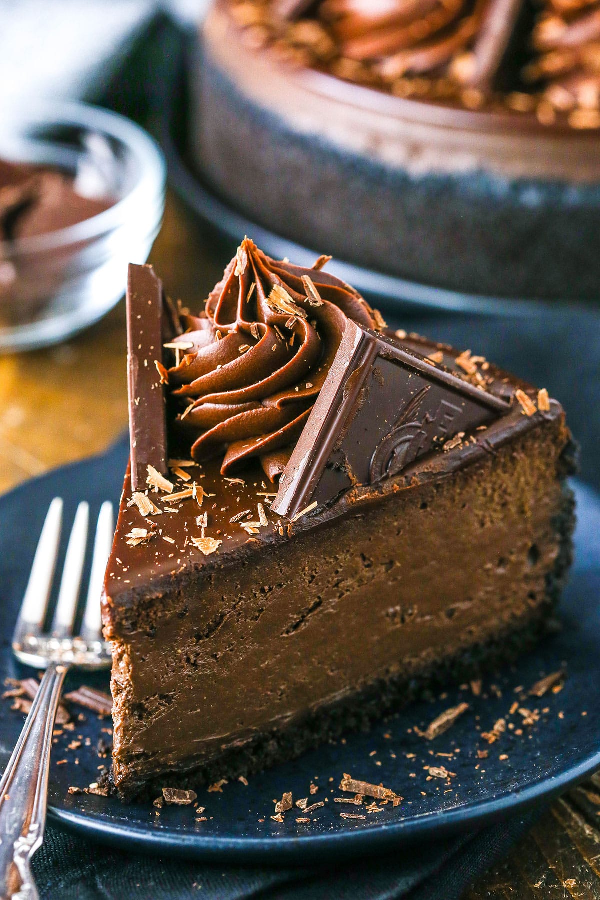 A slice of Decadent Dark Chocolate Cheesecake on a black plate next to a fork