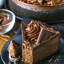 A slice of Decadent Dark Chocolate Cheesecake with a bite removed on a black plate next to a fork