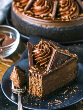 A slice of Decadent Dark Chocolate Cheesecake with a bite removed on a black plate next to a fork