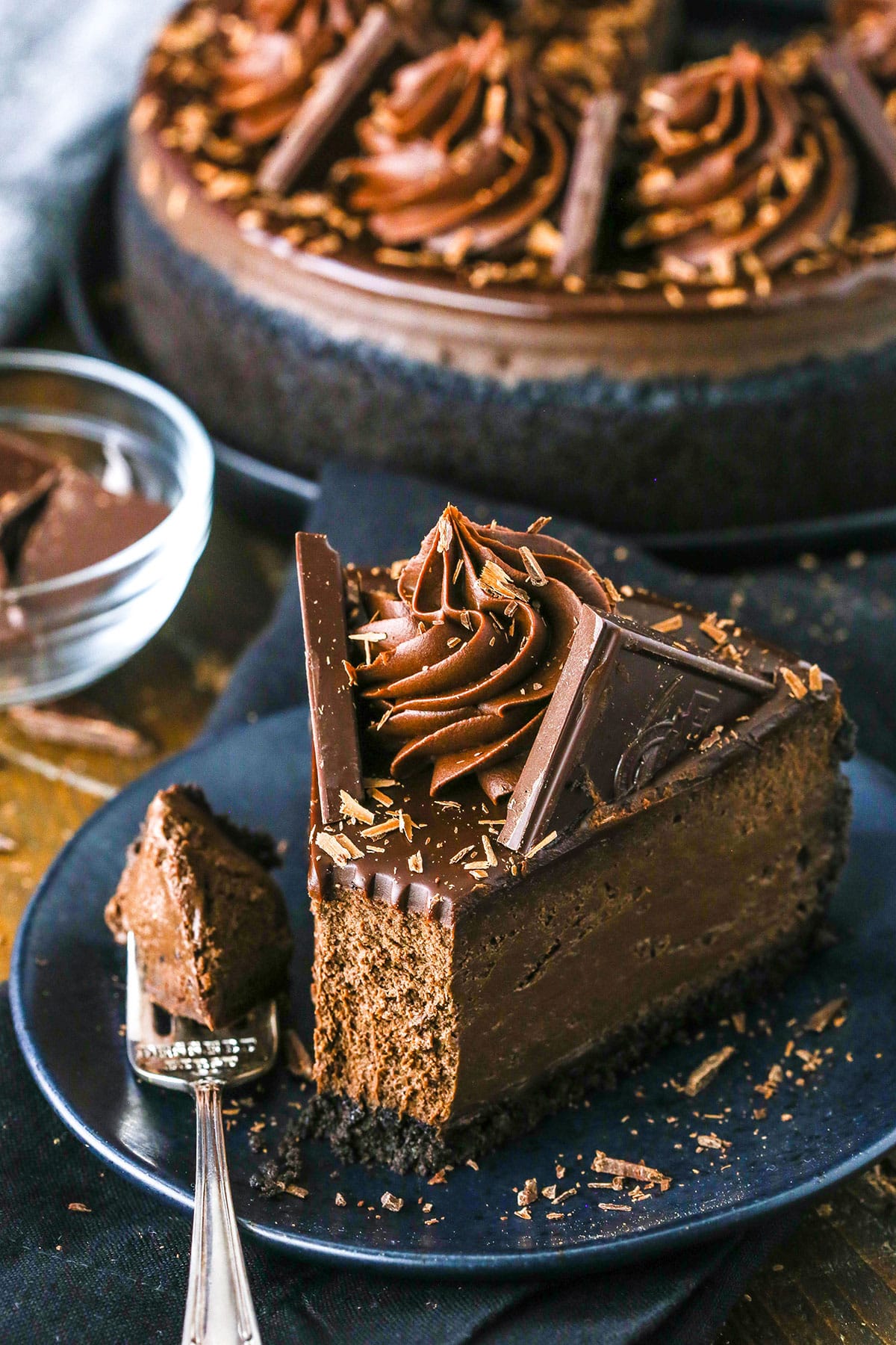 A slice of Decadent Dark Chocolate Cheesecake with a bite removed on a black plate next to a fork