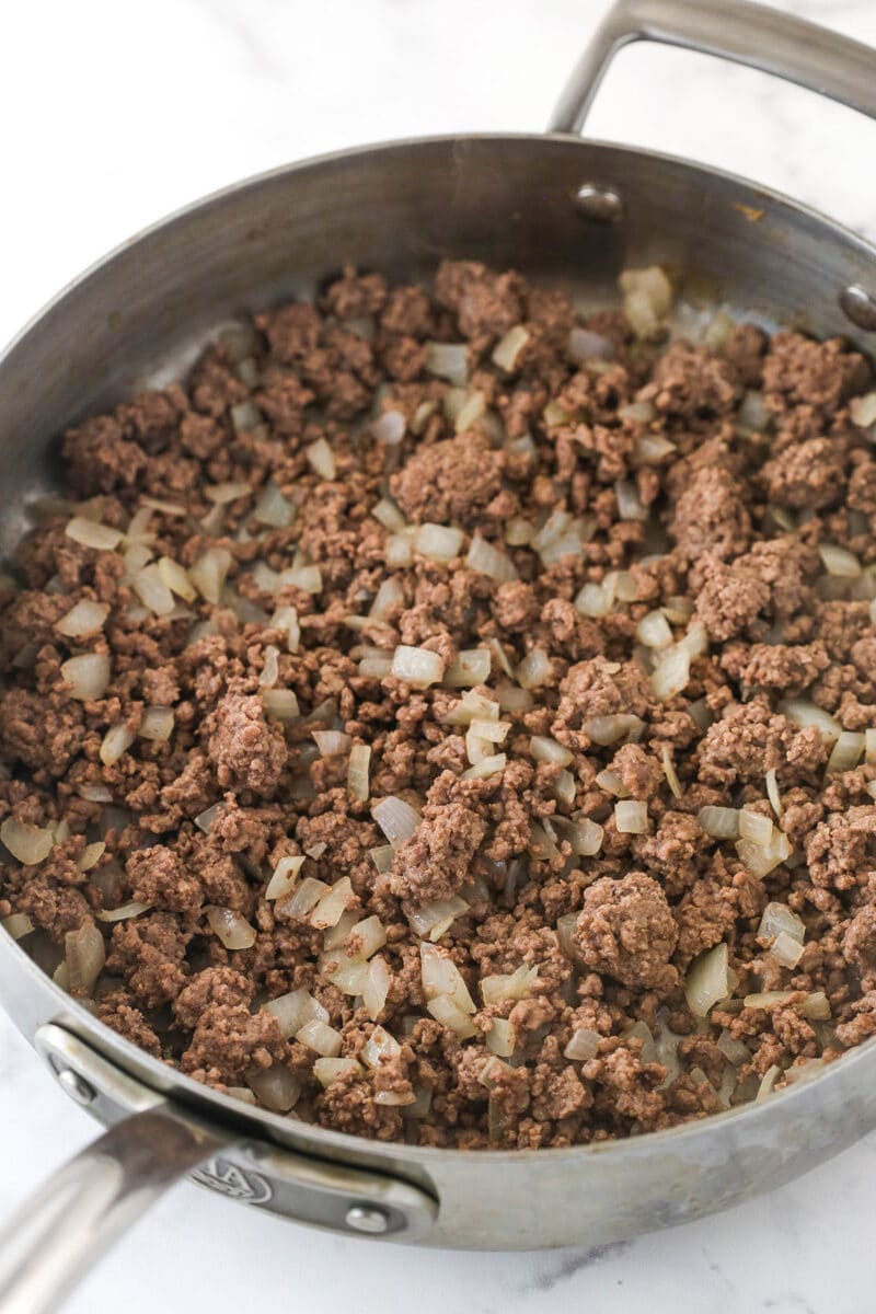 This Dorito casserole is made with layers of Doritos, ground beef, cheese, black beans, and corn and is packed with taco flavor. Cooking ground beef and onions in a pan.