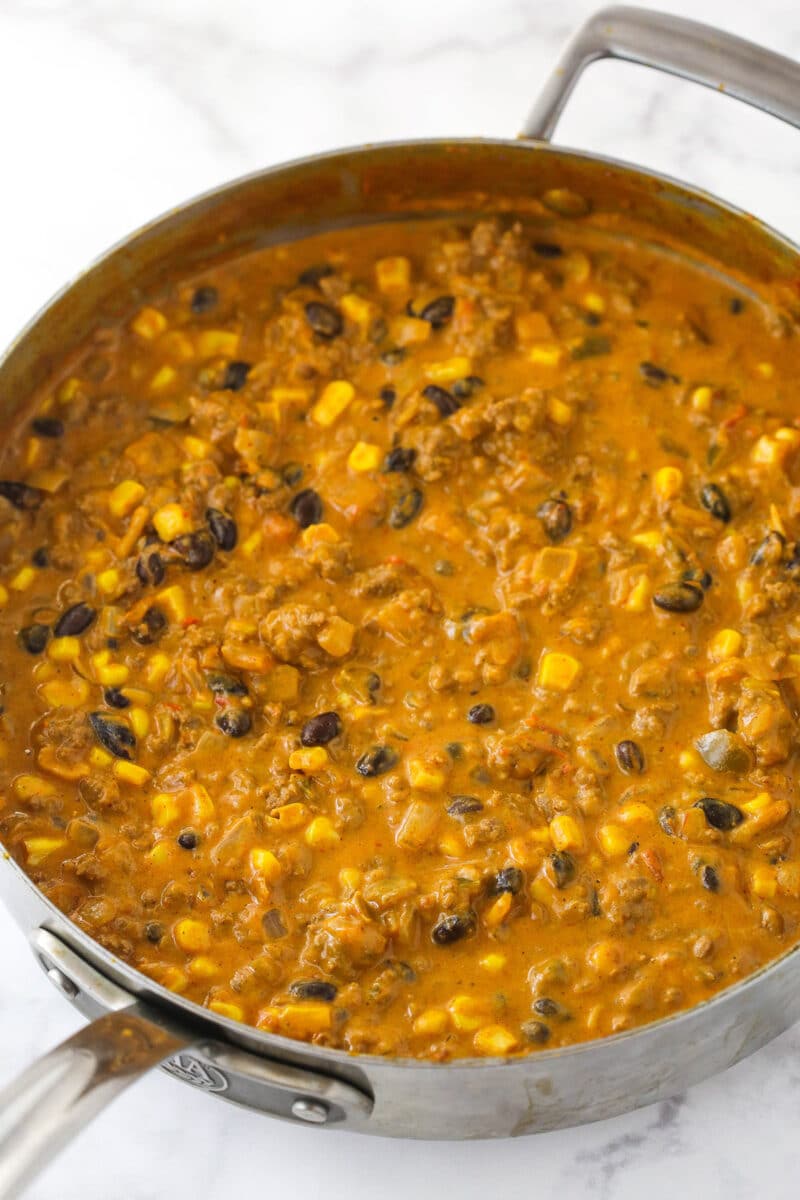 This Dorito casserole is made with layers of Doritos, ground beef, cheese, black beans, and corn and is packed with taco flavor. Filling for Dorito casserole simmering in a sauce pan.