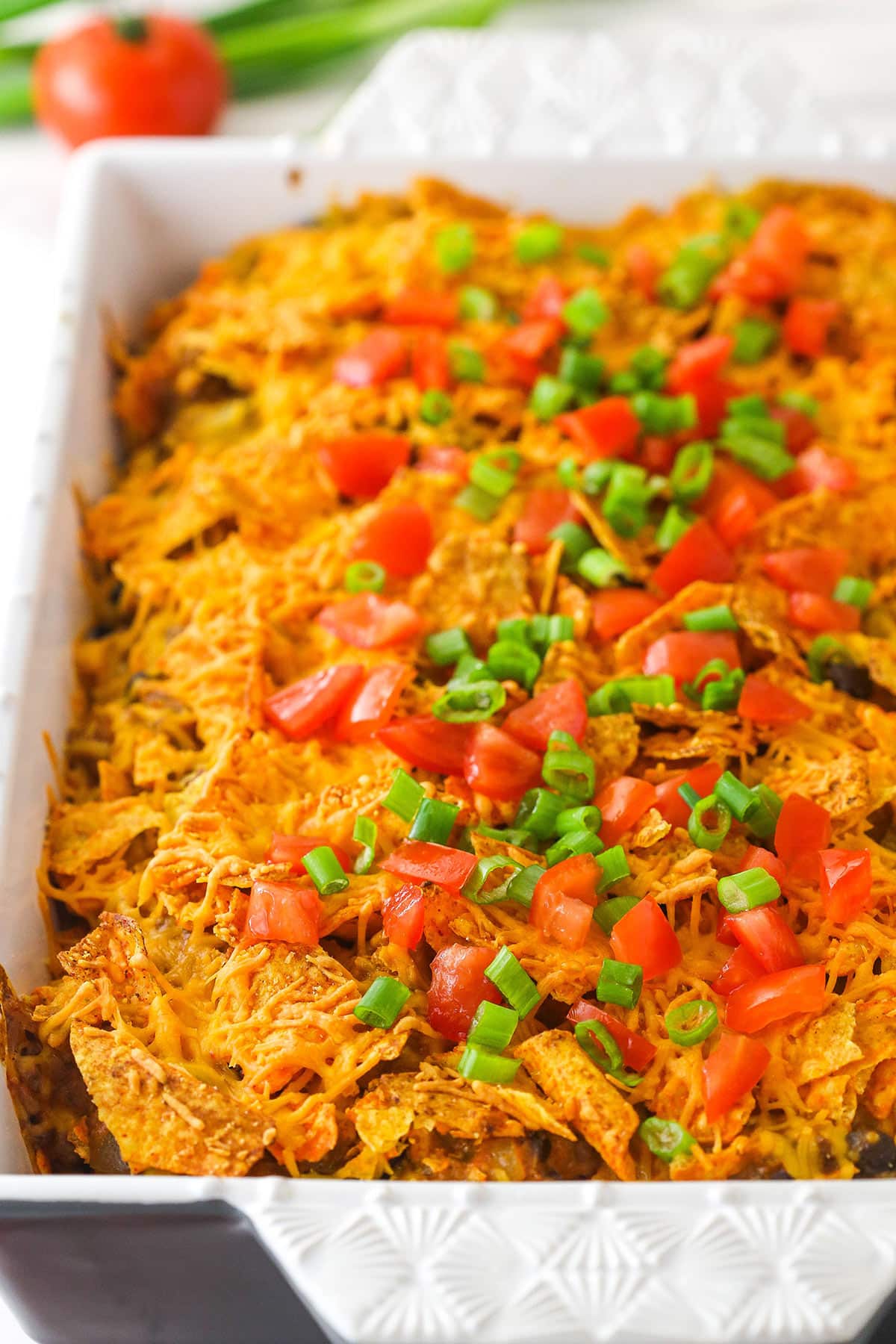 Dorito casserole in a baking pan garnished with tomatoes and green onions.