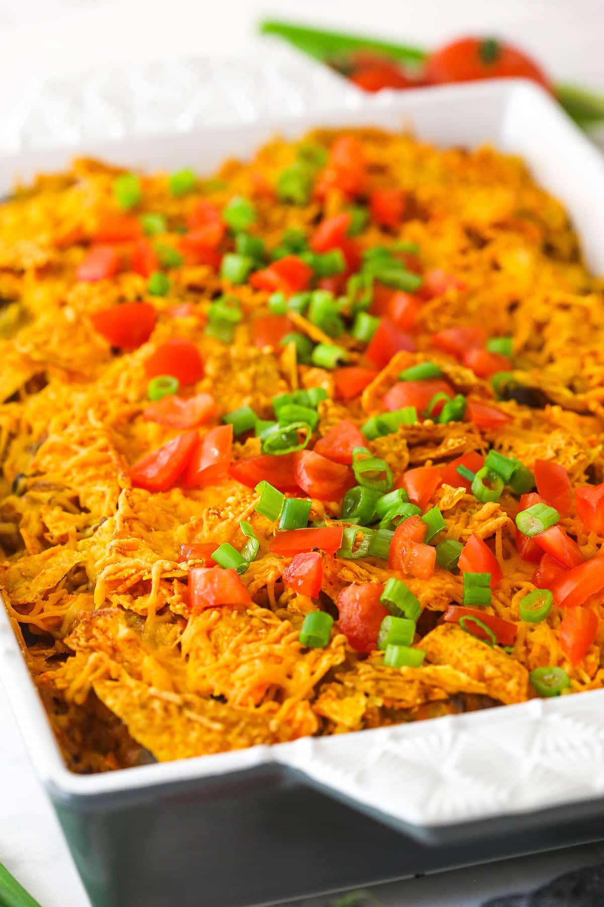 Dorito casserole in a baking pan garnished with tomatoes and green onions.