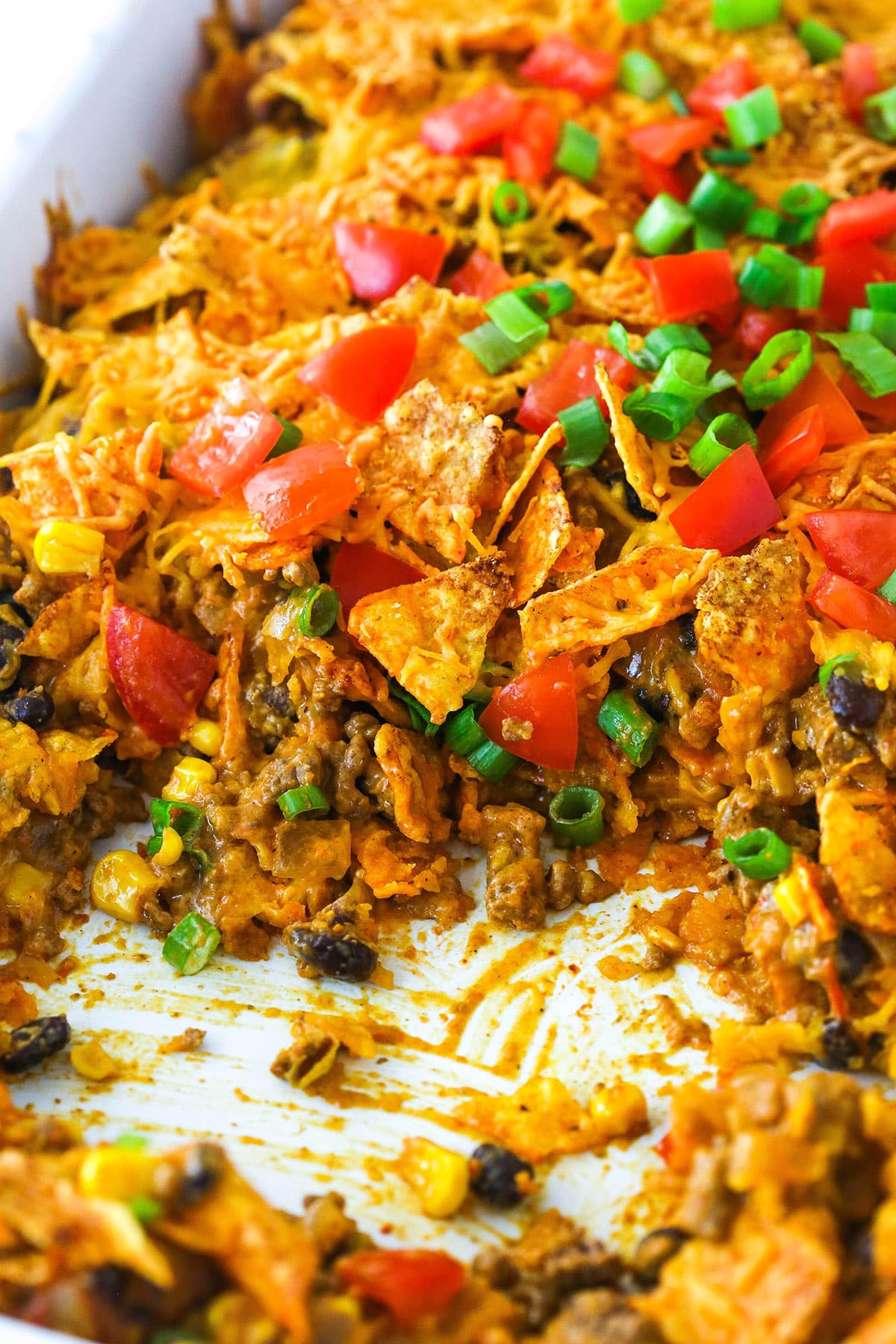 This Dorito casserole is made with layers of Doritos, ground beef, cheese, black beans, and corn and is packed with taco flavor. Dorito casserole in the pan with a slice taken out of it.