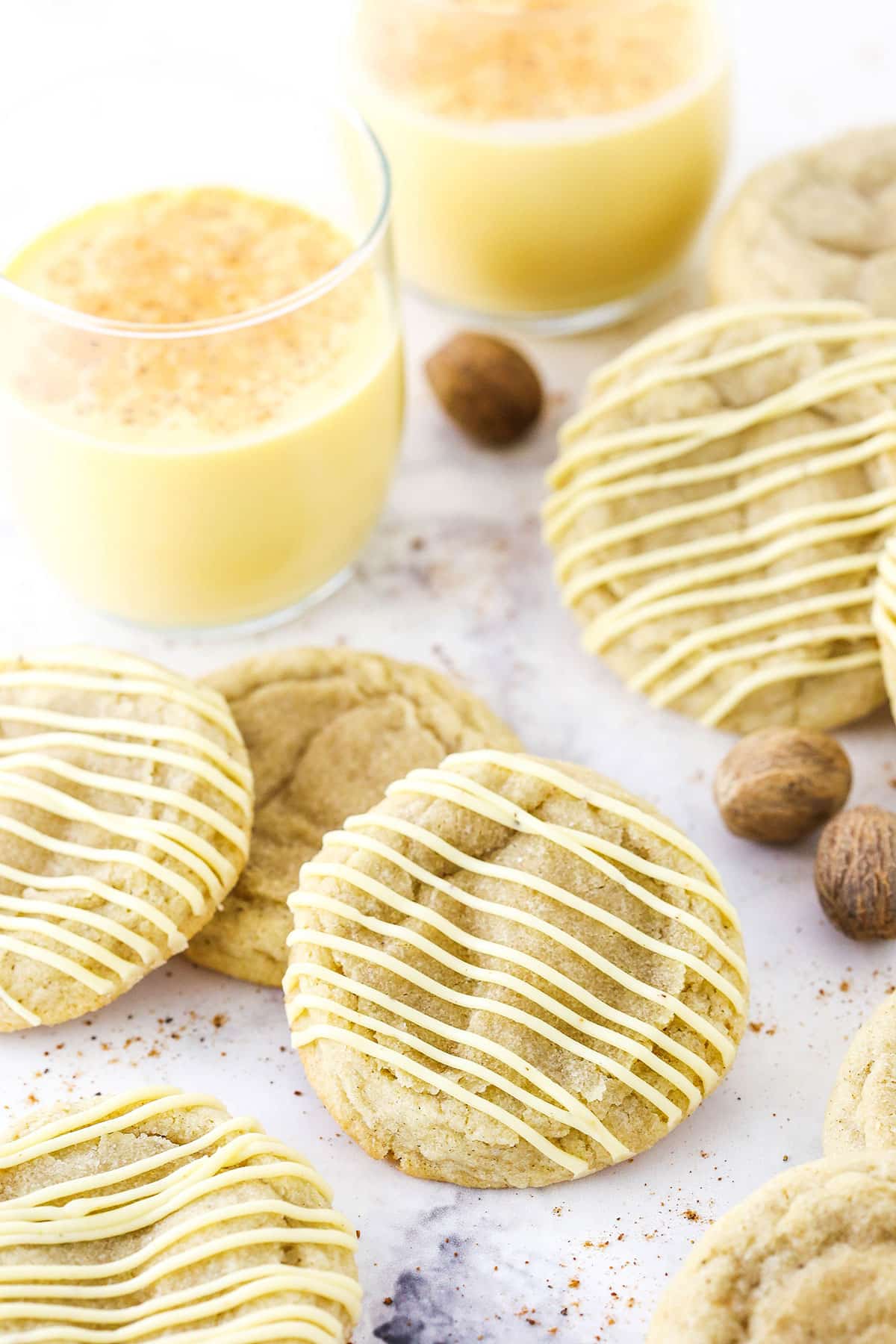 Eggnog Cookies topped with frosting and two glasses of eggnog in the background