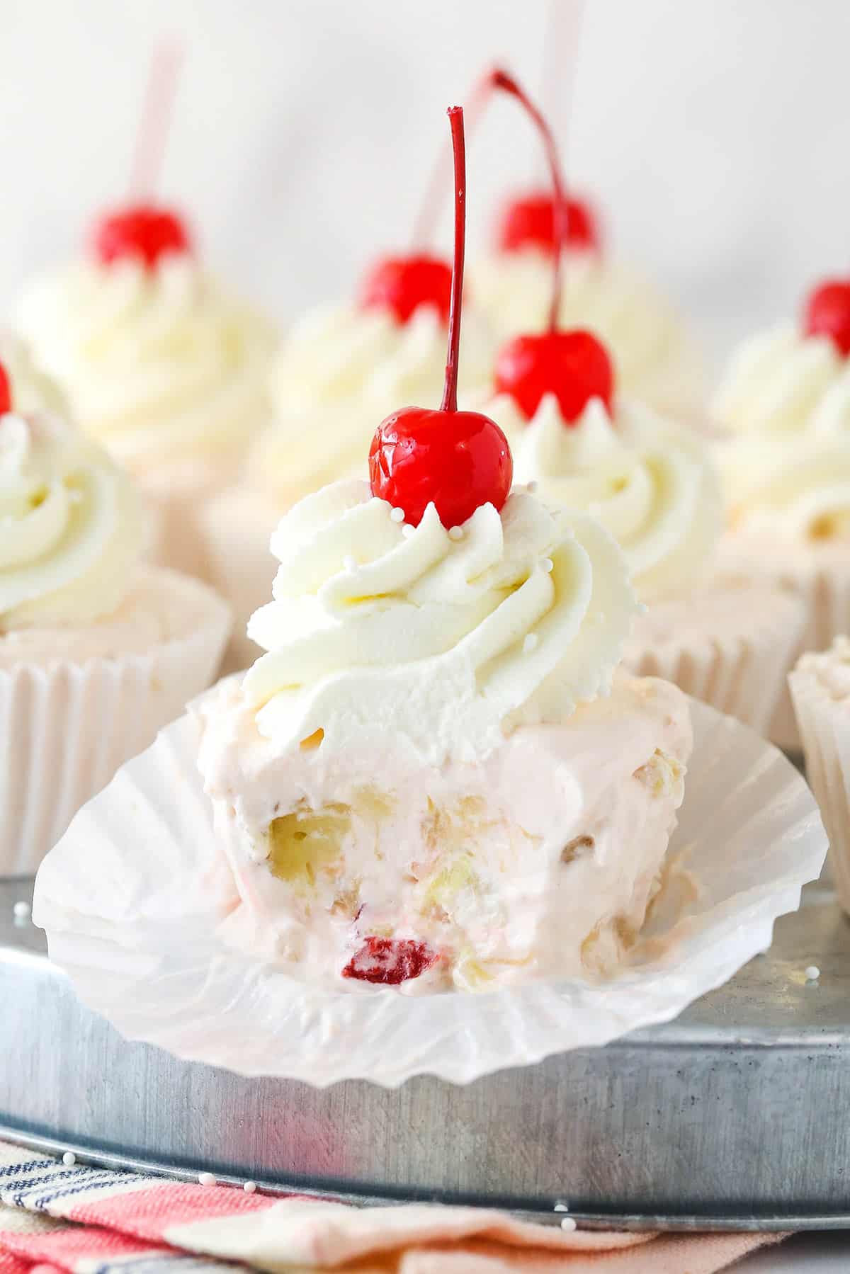 Frozen fruit salad cupcakes are made of cherries, bananas, and pineapples suspended in a creamy, frozen filling. Closeup of a frozen fruit salad cupcake with a bite taken out of it.