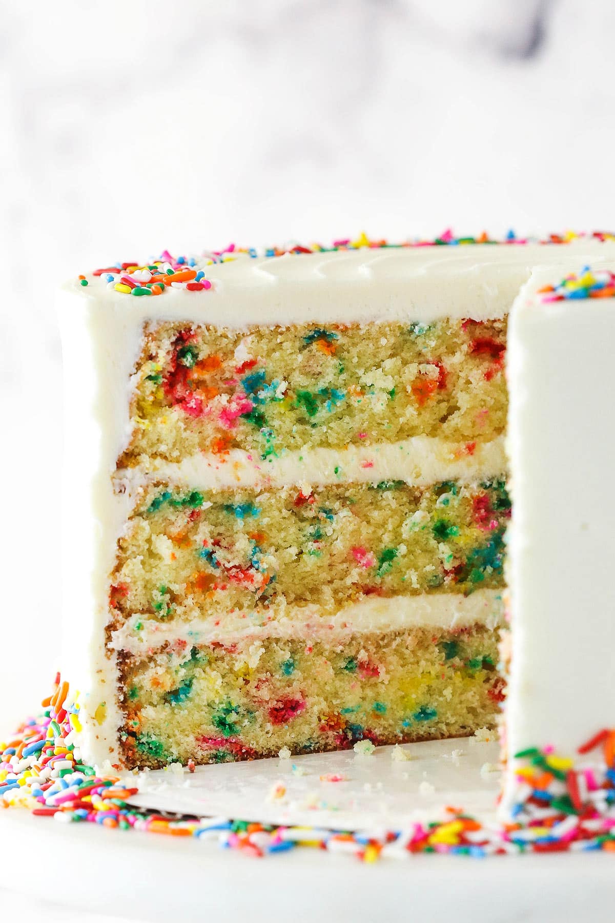 Funfetti cake on a serving platter with a slice taken out of it.