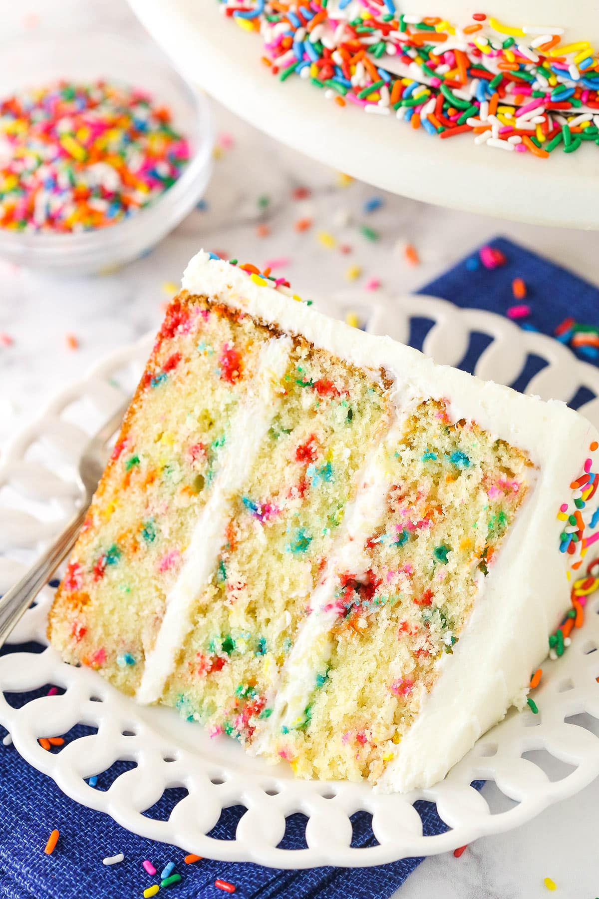 Overhead of a slice of Funfetti layer cake on a plate surrounded by rainbow sprinkles.