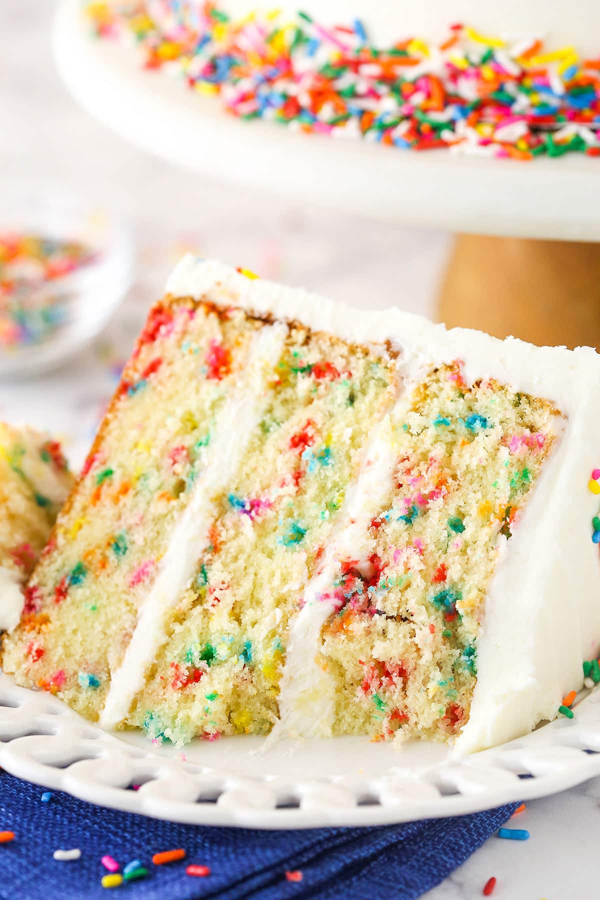 Closeup of a slice of Funfetti layer cake on a plate surrounded by rainbow sprinkles.