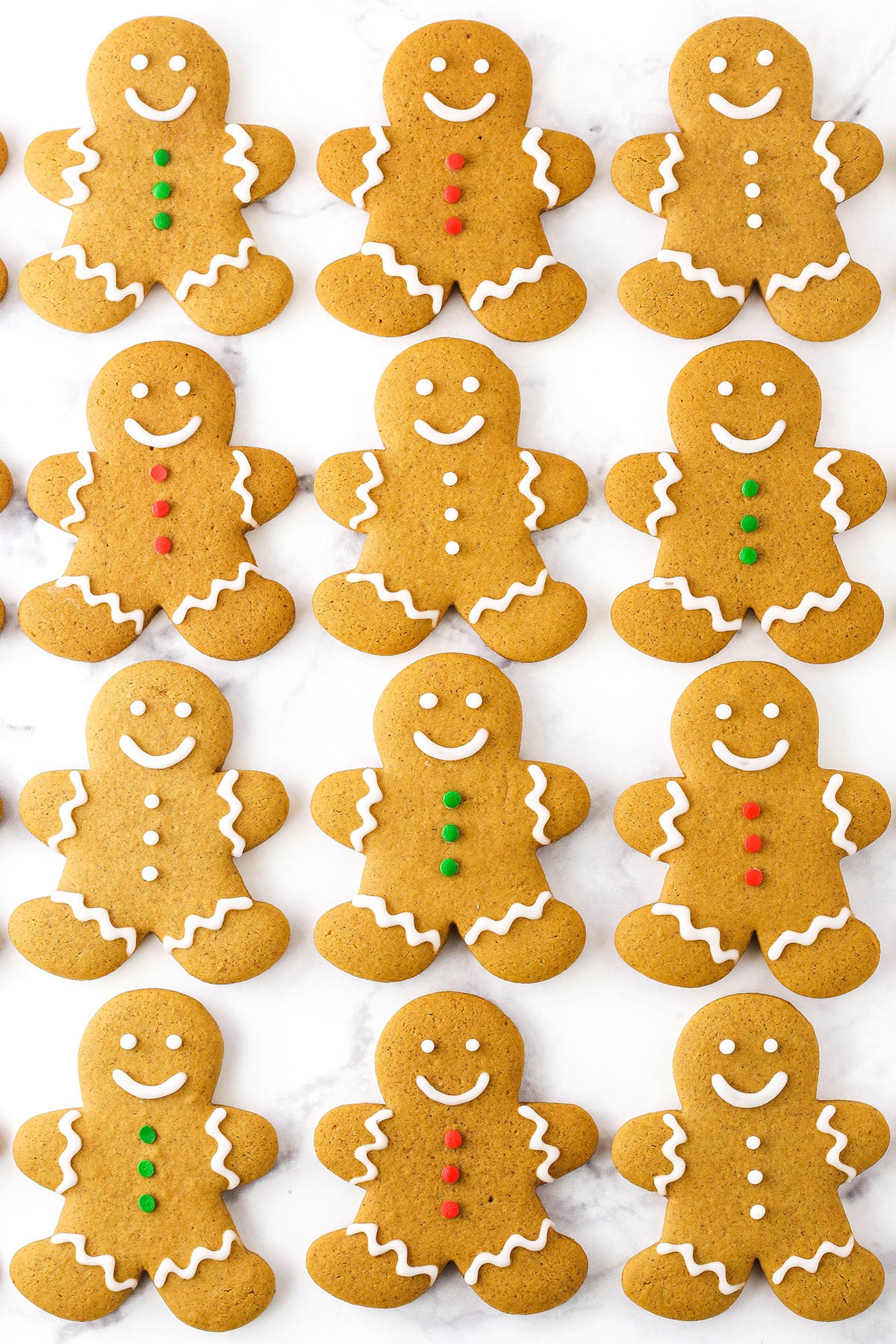 Overhead view of Gingerbread Cookies decorated with white, green and red frosting spread out on a white table