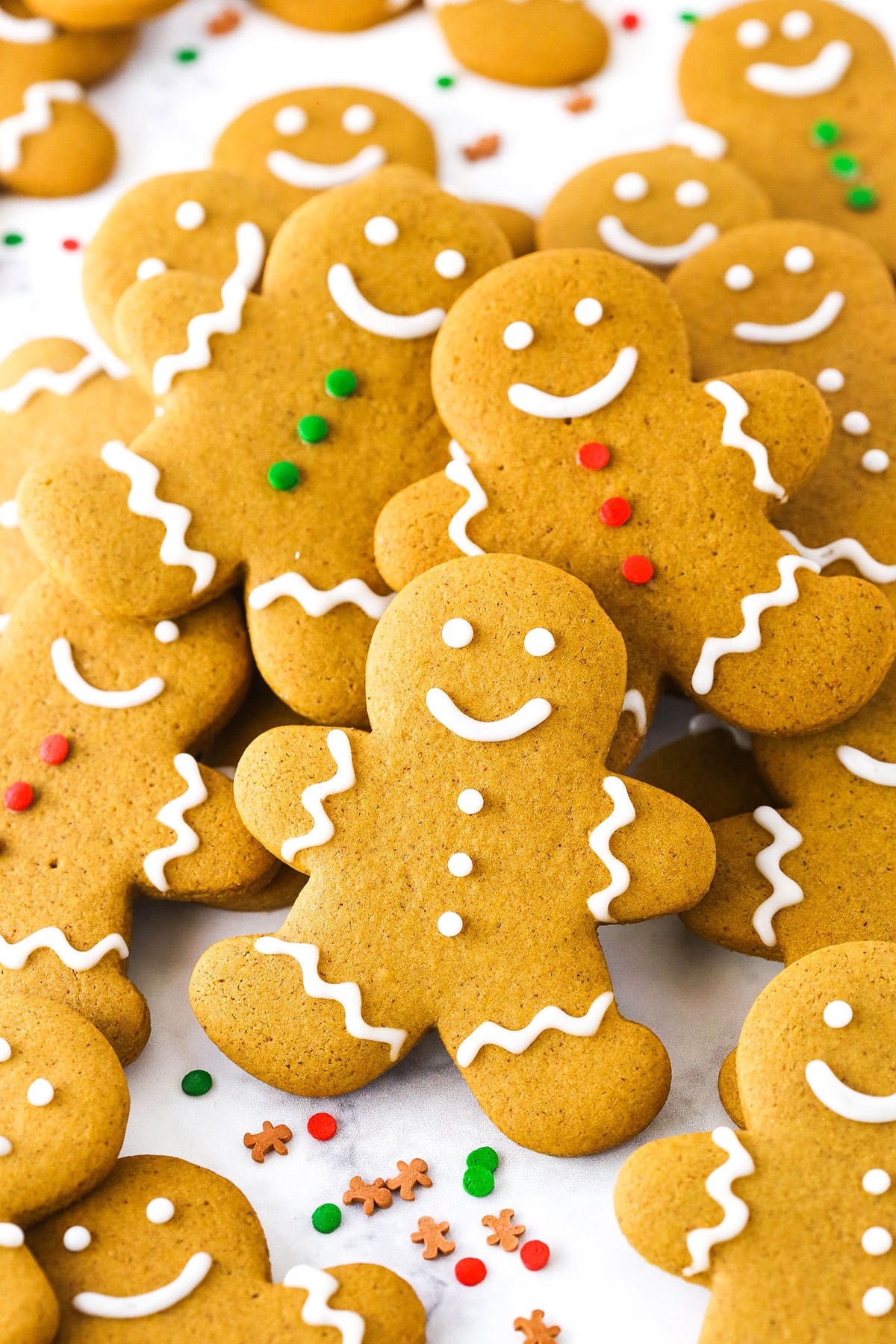 Gingerbread Cookies decorated with white, green and red frosting layered on a white table