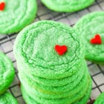 Green Grinch Cookies topped with a small heart shaped sprinkle spread out over a cooling rack on a white table top