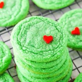 Green Grinch Cookies topped with a small heart shaped sprinkle spread out over a cooling rack on a white table top