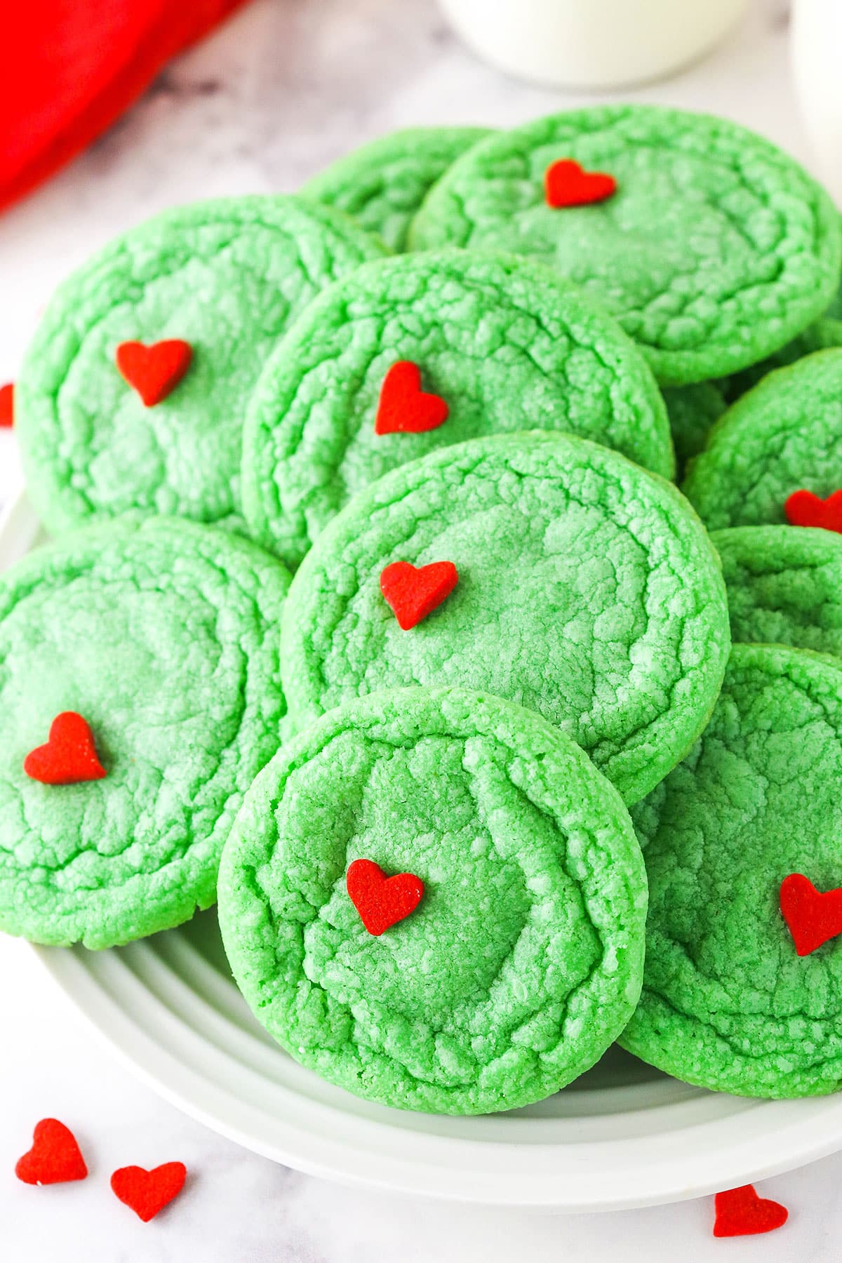 Green Grinch Cookies topped with a small heart shaped sprinkle stacked on a white plate.
