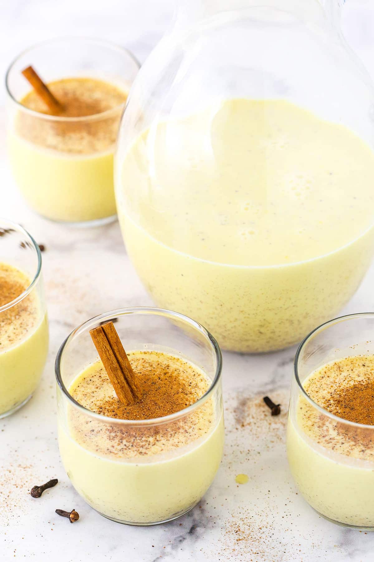 Four glasses of Homemade Eggnog around a glass pitcher with Eggnog