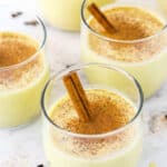 Four glasses of Homemade Eggnog topped with cinnamon with a cinnamon stick
