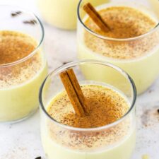 Four glasses of Homemade Eggnog topped with cinnamon with a cinnamon stick