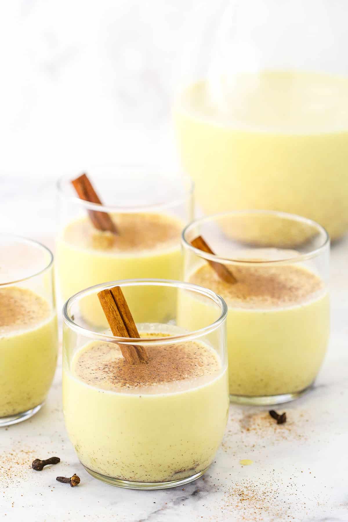 Four glasses of Homemade Eggnog topped with cinnamon with a cinnamon stick