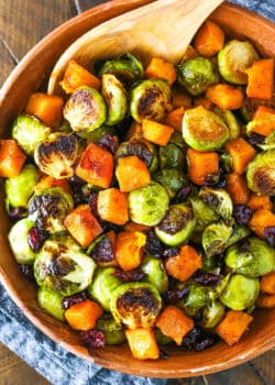 Honey Roasted Brussels Sprouts with Butternut Squash and Cranberries in a wooden serving dish with a wooden spoon
