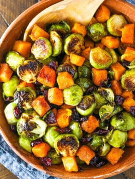 Honey Roasted Brussels Sprouts with Butternut Squash and Cranberries in a wooden serving dish with a wooden spoon