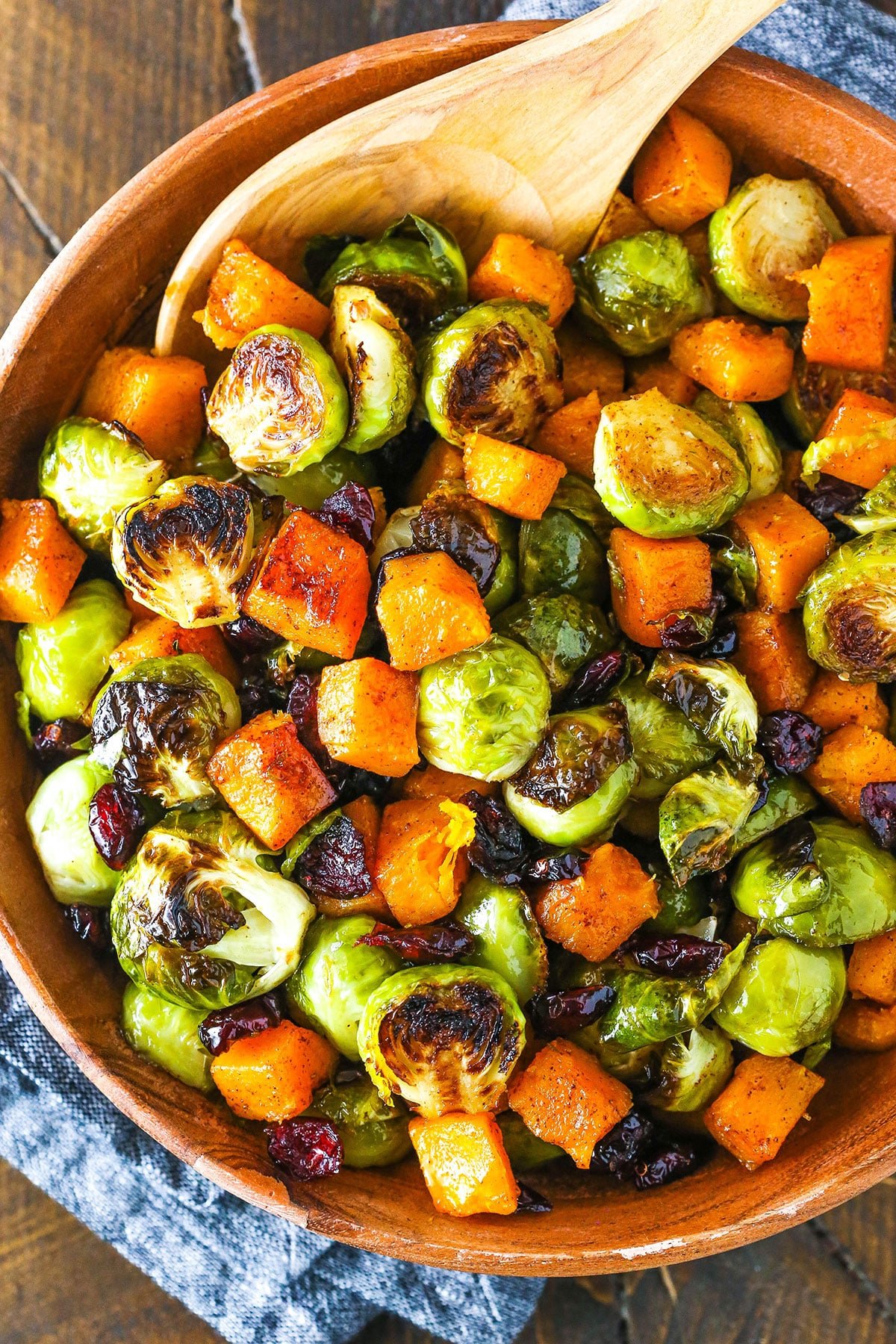 Honey Roasted Brussels Sprouts with Butternut Squash and Cranberries in a wooden serving dish with a wooden spoon