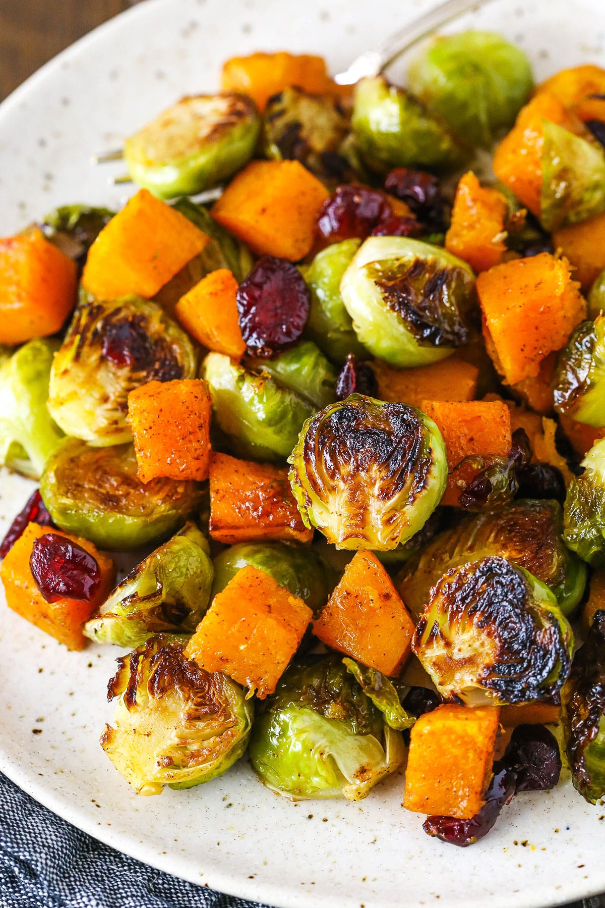 Honey Roasted Brussels Sprouts with Butternut Squash and Cranberries on a white plate with a fork