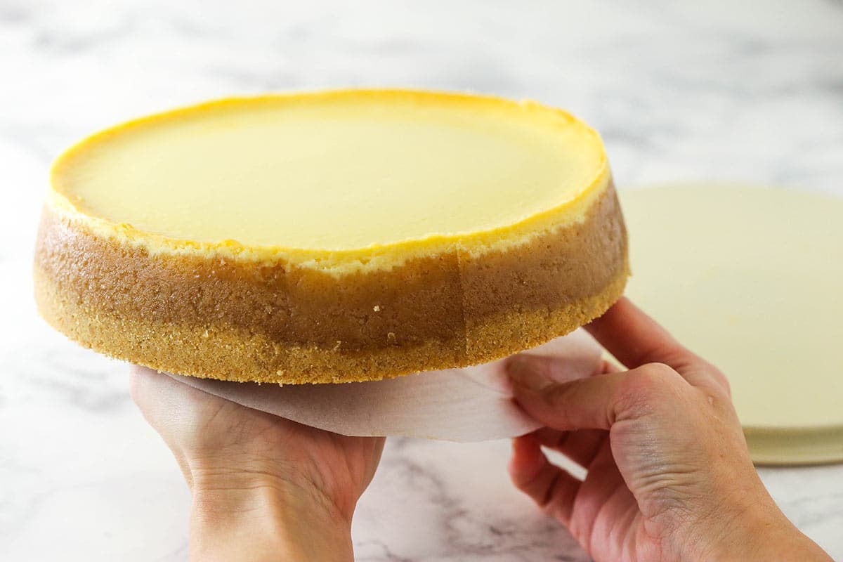 using my right hand to start removing the parchment paper while resting the cheesecake in the palm of my left hand