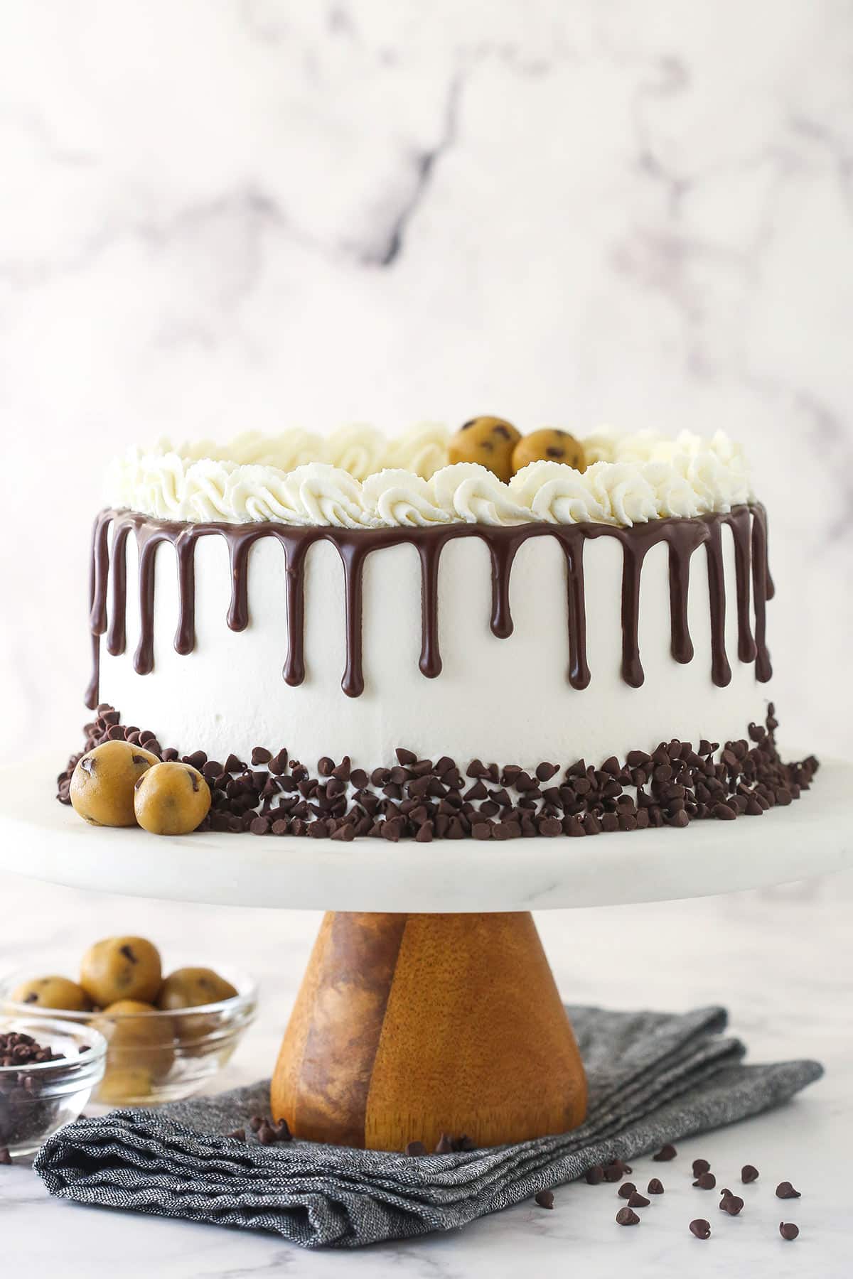 Ice cream cake on a cake stand near cookie dough and chocolate chips.